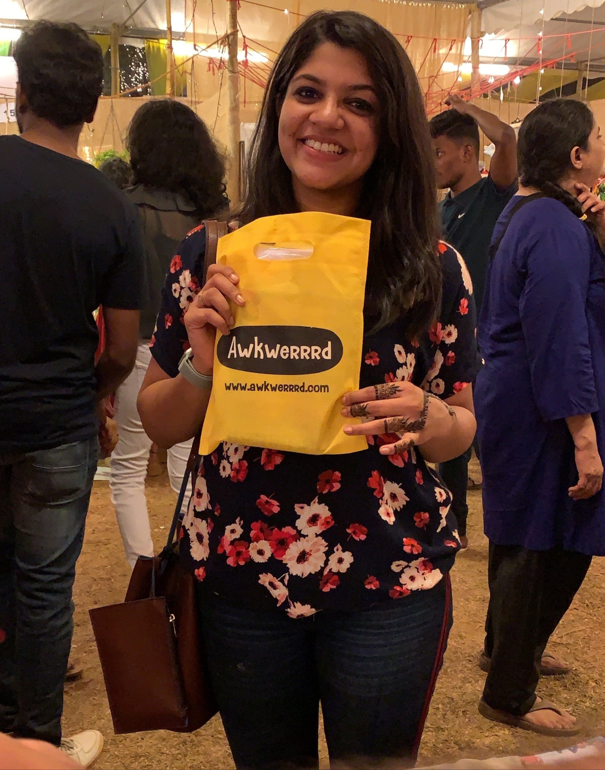 Woman holding a yellow packet with text at an outdoor event.