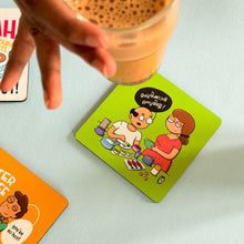 Hand holding a glass of iced coffee above a coaster with cartoon characters on a light surface.