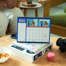 Person sitting at a table with a calendar, bowl of cereal, and camera.